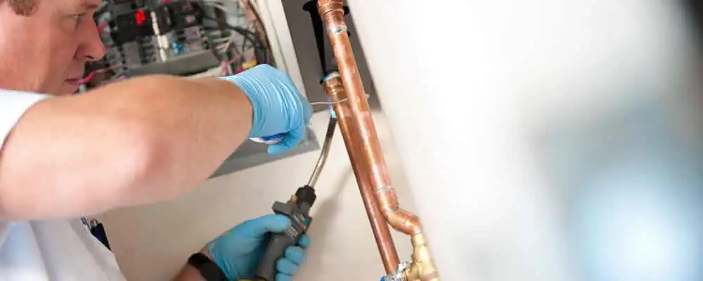 Water heater repair technician testing copper pipe connections and controls in Lancaster, PA